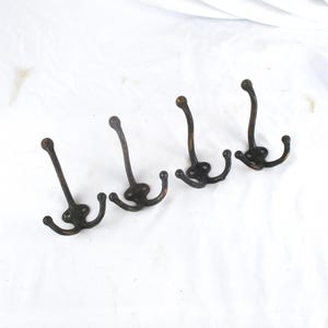 May include: Four dark bronze-toned metal wall hooks, each featuring a central vertical prong and two smaller curved side prongs. Each hook has a circular base plate with two screw holes for mounting, and all prongs end in rounded ball tips.