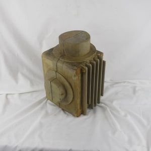 May include: A wooden model of a motor with a rectangular base and a cylindrical top. The model is made of multiple pieces of wood that are joined together. The model is painted a light brown color.