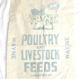 May include: Vintage feed sack with faded blue text and graphics. The text reads "WAYNE POULTRY AND LIVESTOCK FEEDS" with a graphic of a rooster. The sack is made of a light-colored, possibly canvas, material.