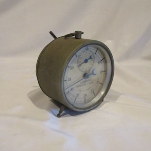 May include: A vintage green metal Hanovia Interval Timer with a white face and black markings. The timer has a large dial with numbers from 5 to 60, and a smaller dial with numbers from 5 to 30. The timer is in good condition and has a few signs of wear.