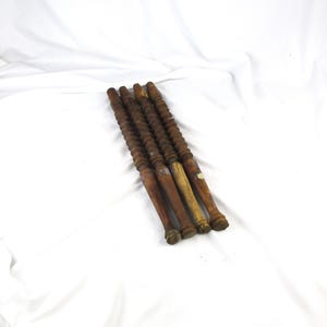 May include: A collection of five antique wooden spindles, each with a turned, spiral-grooved shaft and a rounded handle. The spindles vary in color from light to dark brown, with some showing signs of age and wear. They are arranged diagonally against a white background.