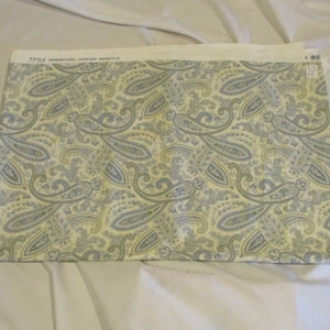 May include: A fabric swatch with a paisley pattern in shades of blue and yellow. The fabric has a white background and the paisley pattern is repeated throughout the fabric. The fabric is labeled "TP54 INTERNATIONAL COMFORT FABRIC"