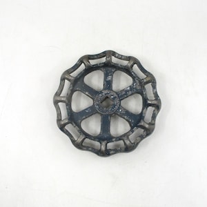 May include: A circular, cast iron valve handle with a dark blue finish. The handle has a spoke-like design with an open center and a square hole. The metal shows signs of wear and age.