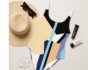 Peut inclure: Maillot de bain une pièce avec un motif géométrique noir, blanc, bleu clair, pêche et jaune. Un chapeau de soleil en paille, des lunettes de soleil noires, de la crème solaire et un coquillage sont également présents.