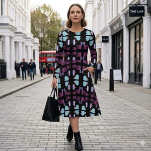 May include: A long-sleeved dress with a black background and a geometric pattern in shades of purple and teal. The dress has a round neckline and pockets. A black tote bag is held in the left hand.