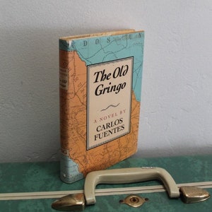May include: A vintage paperback book titled "The Old Gringo" by Carlos Fuentes. The cover features a map with a blue and green color scheme.