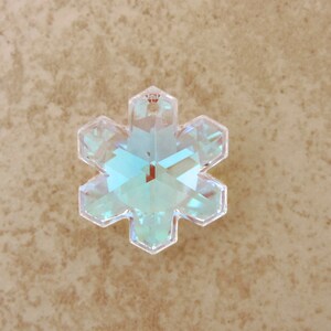 Peut inclure: Un pendentif en cristal clair en forme de flocon de neige iris&eacute;. Le pendentif a six pointes et un trou en haut pour l'accrocher. Le cristal refl&egrave;te la lumi&egrave;re, affichant une gamme de couleurs dont le bleu, le vert et le jaune. Id&eacute;al pour la fabrication de bijoux ou les d&eacute;corations de f&ecirc;tes.