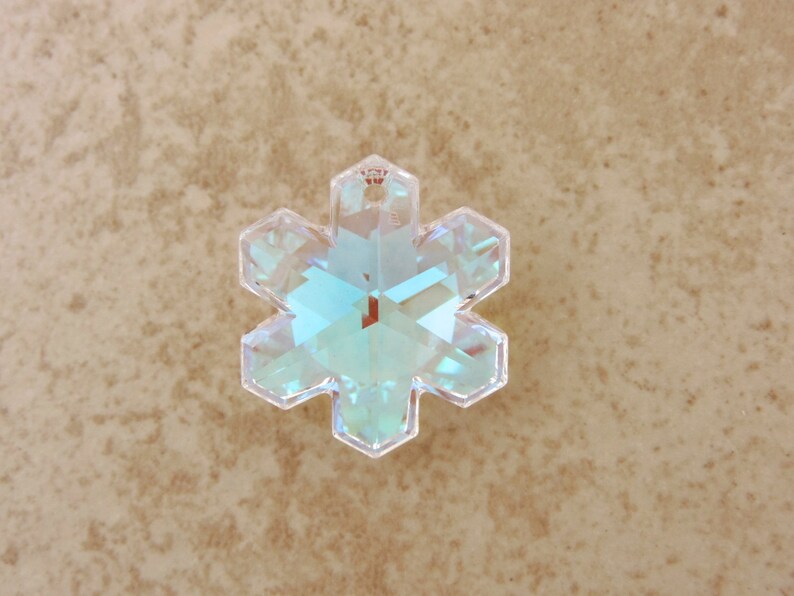 Peut inclure: Un pendentif en cristal clair en forme de flocon de neige iris&eacute;. Le pendentif a six pointes et un trou en haut pour l'accrocher. Le cristal refl&egrave;te la lumi&egrave;re, affichant une gamme de couleurs dont le bleu, le vert et le jaune. Id&eacute;al pour la fabrication de bijoux ou les d&eacute;corations de f&ecirc;tes.