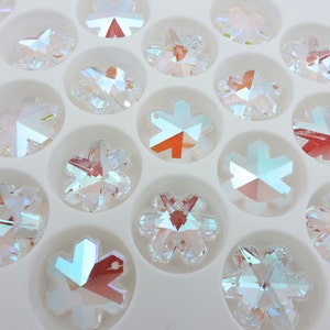 Peut inclure: Gros plan sur des cristaux transparents iris&eacute;s en forme de flocons de neige dispos&eacute;s dans un plateau blanc. Les cristaux ont de multiples facettes qui r&eacute;fl&eacute;chissent la lumi&egrave;re, cr&eacute;ant un effet arc-en-ciel.