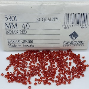 May include: A collection of small, faceted Indian Red Swarovski crystal beads, 4.0 mm in size, displayed in front of their original white paper packaging. The packaging features the text 5301, 1st QUALITY, MM 4,0, INDIAN RED, and SWAROVSKI COMPONENTS.