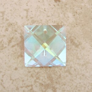 Puede incluir: Un colgante cuadrado de cristal iridiscente con un agujero para ensartar. El cristal presenta un patr&oacute;n geom&eacute;trico en forma de diamante, que refleja un espectro de colores. Adecuado para la creaci&oacute;n de joyas o proyectos de artesan&iacute;a. Mide aproximadamente 2,5 cm x 2,5 cm.