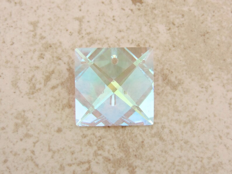 Puede incluir: Un colgante cuadrado de cristal iridiscente con un agujero para ensartar. El cristal presenta un patr&oacute;n geom&eacute;trico en forma de diamante, que refleja un espectro de colores. Adecuado para la creaci&oacute;n de joyas o proyectos de artesan&iacute;a. Mide aproximadamente 2,5 cm x 2,5 cm.
