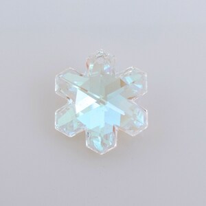 Peut inclure: Pendentif en cristal clair en forme de flocon de neige facett&eacute;. Le pendentif a six pointes et refl&egrave;te un arc-en-ciel de couleurs. Le cristal est suspendu sur un fond blanc uni. Id&eacute;al pour la fabrication de bijoux ou la d&eacute;coration de vacances.