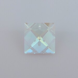 Puede incluir: Un colgante cuadrado de cristal iridiscente con un dise&ntilde;o facetado. El colgante tiene un peque&ntilde;o agujero en la parte superior para colgarlo. El cristal refleja una gama de colores, incluyendo azul, verde y amarillo.