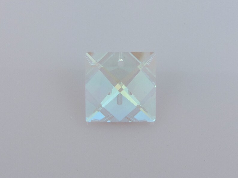 Puede incluir: Un colgante cuadrado de cristal iridiscente con un dise&ntilde;o facetado. El colgante tiene un peque&ntilde;o agujero en la parte superior para colgarlo. El cristal refleja una gama de colores, incluyendo azul, verde y amarillo.
