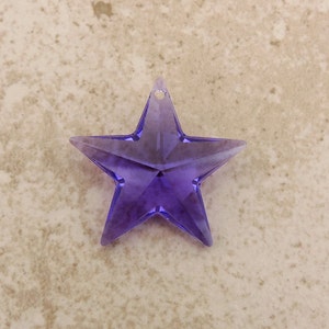 May include: A purple, star-shaped ornament with a small hole for hanging. The star is made of a translucent material, with facets that catch the light. This decorative item is ideal for festive occasions or as a unique home decor piece.