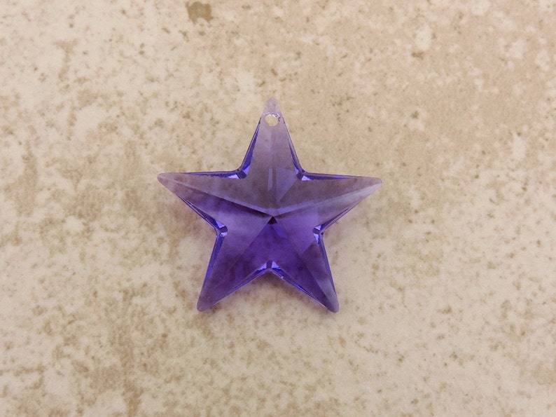 May include: A purple, star-shaped ornament with a small hole for hanging. The star is made of a translucent material, with facets that catch the light. This decorative item is ideal for festive occasions or as a unique home decor piece.