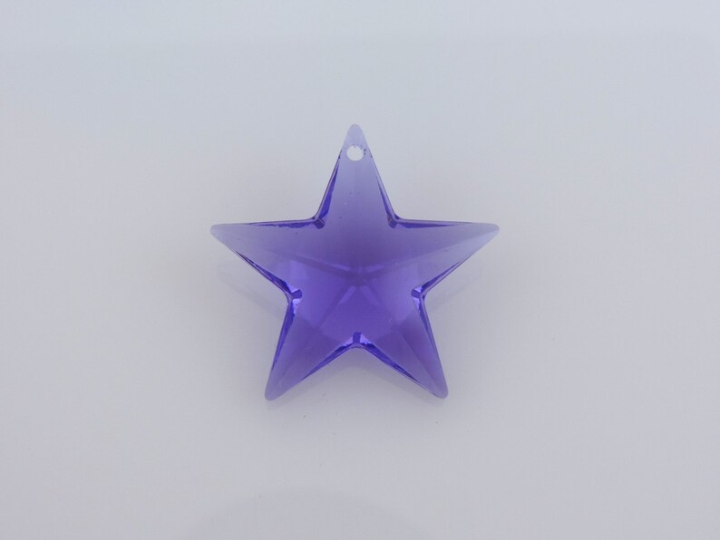May include: A translucent, purple star-shaped ornament with a small hole for hanging. The star has five points and is made of a clear, shiny material. The ornament is set against a plain white background.