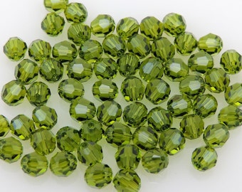 Puede incluir: Cuentas de vidrio facetadas de color verde oliva sobre una superficie blanca. Las cuentas tienen múltiples facetas que reflejan la luz. Adecuadas para la creación de joyas y manualidades.
