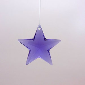 May include: A hanging, faceted, purple star ornament. The star is suspended by a thin, white string. The star has a hole at the top for hanging and is made of a translucent material.