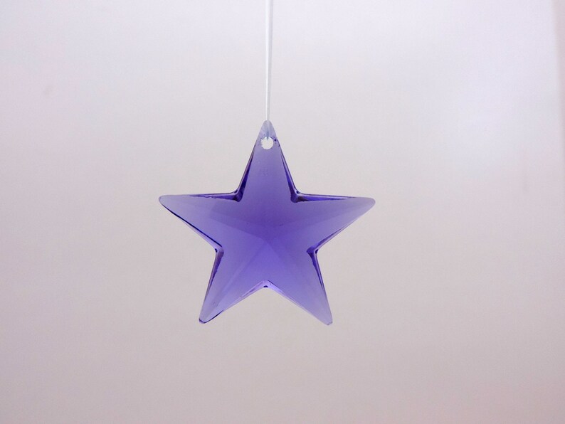 May include: A hanging, faceted, purple star ornament. The star is suspended by a thin, white string. The star has a hole at the top for hanging and is made of a translucent material.