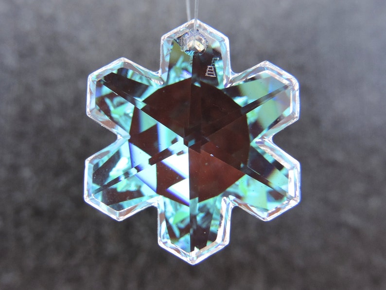 Peut inclure: Ornement en forme de flocon de neige clair et facett&eacute;, &agrave; six pointes. L'ornement pr&eacute;sente un motif g&eacute;om&eacute;trique central brun fonc&eacute; et refl&egrave;te des nuances de bleu et de vert. Une petite boucle est situ&eacute;e en haut pour l'accrocher.