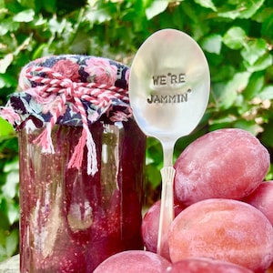 Könnte beinhalten: Ein Glas gefüllt mit roter Marmelade, ein silberner Löffel mit der Gravur "We're Jammin'" und eine Traube roter Trauben.