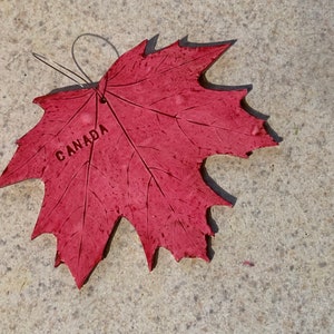 K&ouml;nnte beinhalten: Ein roter Ahornblatt-Anh&auml;nger mit der Aufschrift "CANADA".