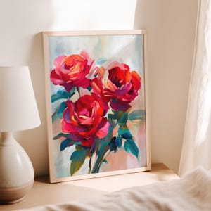 May include: A framed art print featuring a vibrant bouquet of red roses. The painting showcases bold brushstrokes and a palette of red, pink, and green hues. The artwork is displayed in a light-colored wooden frame, leaning against a wall.