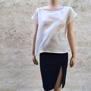 K&ouml;nnte beinhalten: Eine wei&szlig;e, halbtransparente Bluse mit kurzen &Auml;rmeln und einem runden Ausschnitt, kombiniert mit einem dunkelblauen Rock mit Schlitz vorne.