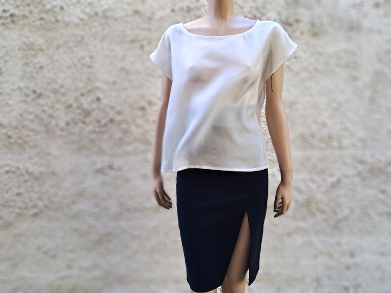 K&ouml;nnte beinhalten: Eine wei&szlig;e, halbtransparente Bluse mit kurzen &Auml;rmeln und einem runden Ausschnitt, kombiniert mit einem dunkelblauen Rock mit Schlitz vorne.