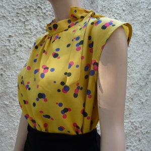 May include: A yellow sleeveless blouse with a high neck and a polka dot pattern in black, pink, and blue.