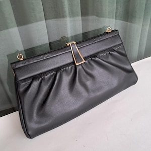 Puede incluir: Un bolso de mano de cuero negro con un cierre dorado. El bolso tiene un diseño fruncido y una correa de cadena.