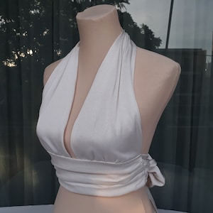 May include: White halter top with a deep V-neck and a wrap-around design. The top is made of a soft, silky fabric and has a relaxed fit.
