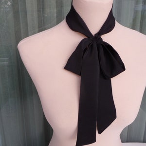 May include: A black satin necktie with a bow tied at the front. The tie is on a white mannequin.