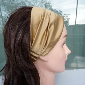 May include: A gold satin headband with a simple design. The headband is folded over and has a smooth, silky texture.