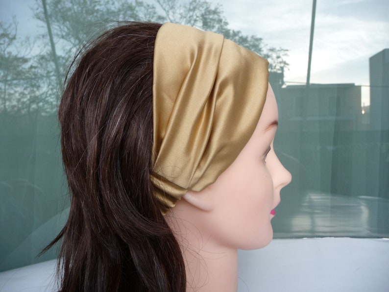 May include: A gold satin headband with a simple design. The headband is folded over and has a smooth, silky texture.