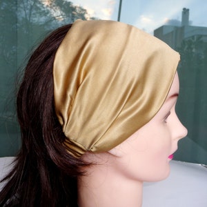 May include: A gold satin headband for hair. The headband is folded and worn on the head of a person with long brown hair.