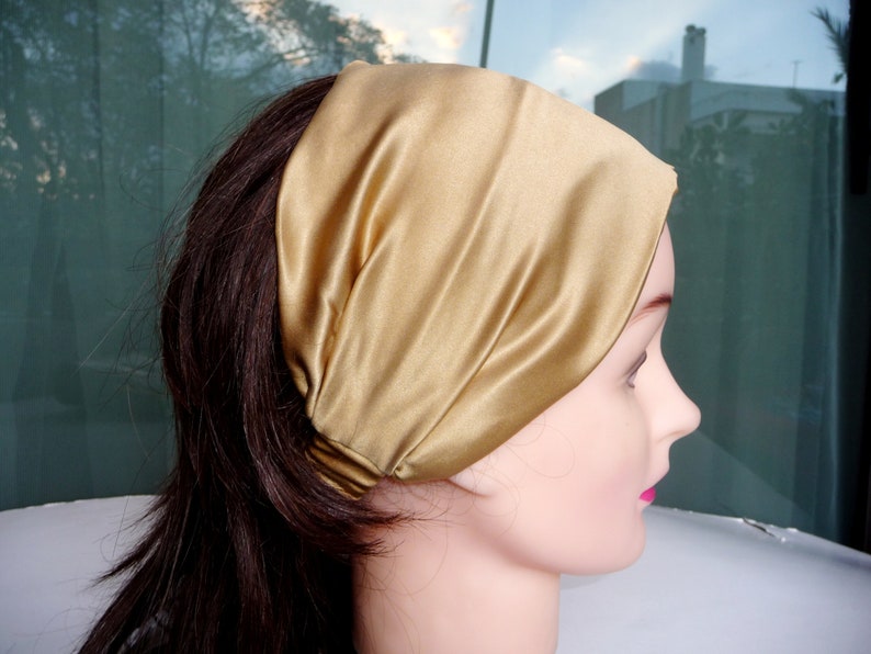 May include: A gold satin headband for hair. The headband is folded and worn on the head of a person with long brown hair.