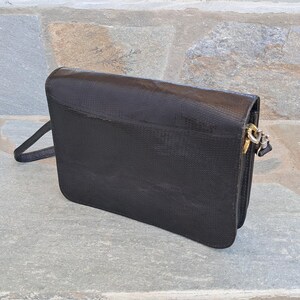 Può includere: Una borsa a tracolla in pelle nera con una superficie testurizzata e una chiusura argentata.
