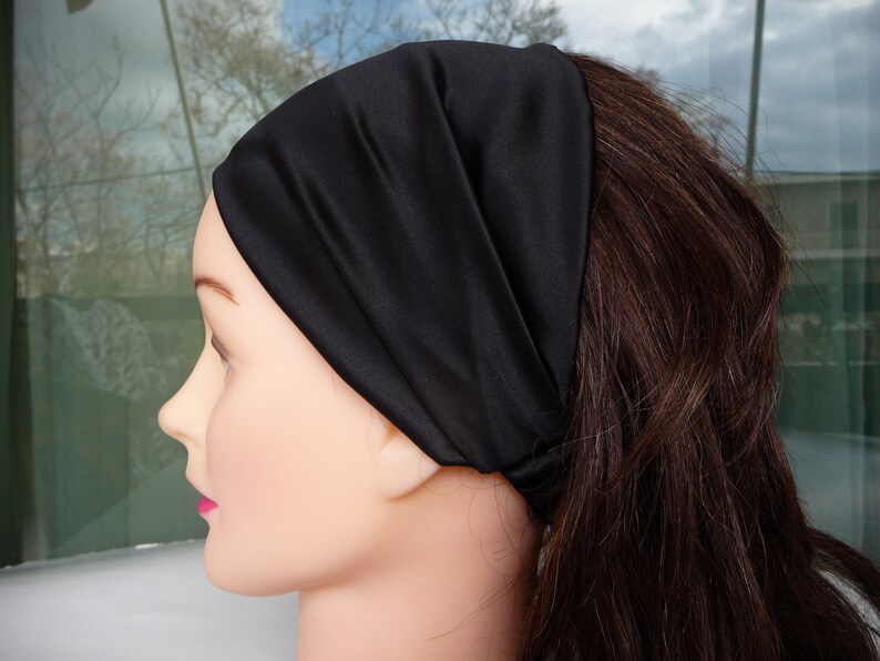 May include: A black satin headband for hair. The headband is worn on a mannequin with long brown hair.