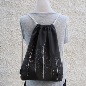 Peut inclure: Un sac à dos noir en tissu avec des silhouettes d'arbres blanches imprimées sur le devant.