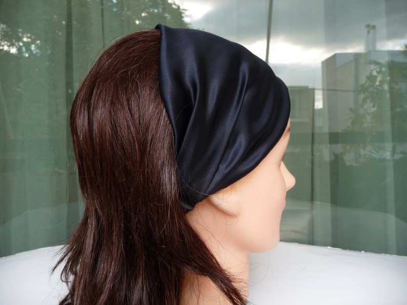May include: A black satin headband worn on a person's head. The headband is folded over and has a smooth, silky texture.
