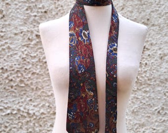 May include: A dark green, red, and blue patterned silk tie with a paisley design. The tie is on a white mannequin.