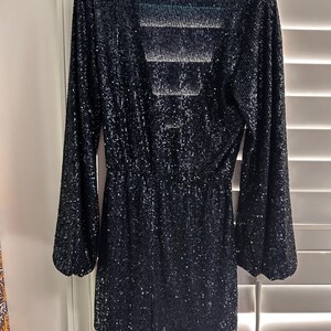 May include: A black sequined long-sleeved dress with a V-neckline and a tie at the waist.