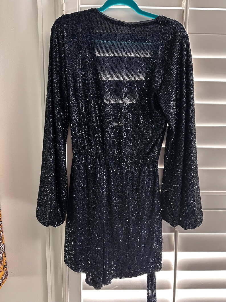 May include: A black sequined long-sleeved dress with a V-neckline and a tie at the waist.