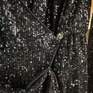 May include: A black sequined dress with a wrap-style bodice and a button closure. The dress is made of a sheer fabric with sequins that shimmer in the light.