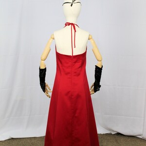 May include: A red halter-style maxi dress with a simple design. The dress is on a mannequin with wooden arms and a black headband.