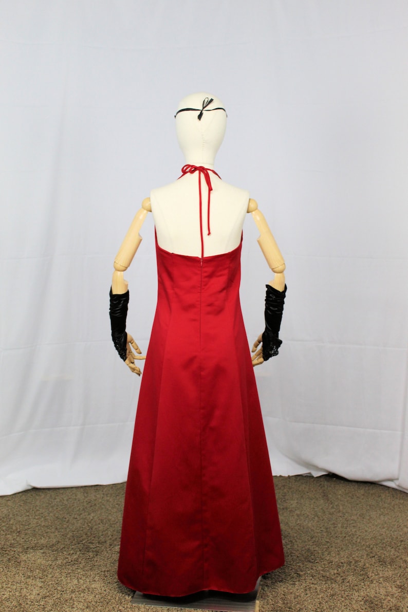 May include: A red halter-style maxi dress with a simple design. The dress is on a mannequin with wooden arms and a black headband.