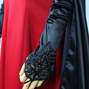 May include: A long black satin glove with a black lace and beaded trim. The glove is worn on a wooden hand.